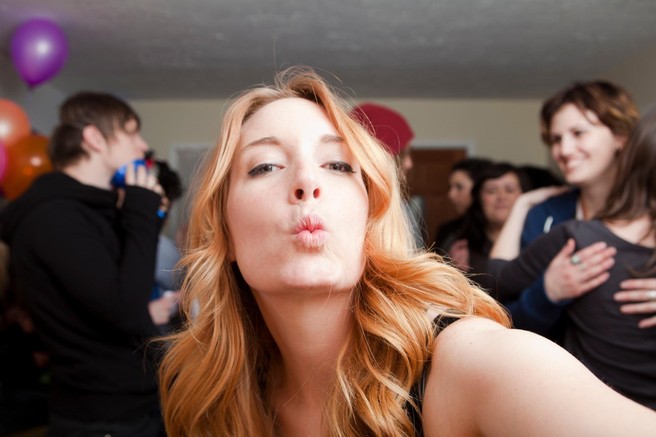Ženska dela selfie z našobljenimi ustnicami. V ozadju so ljudje na zabavi.
