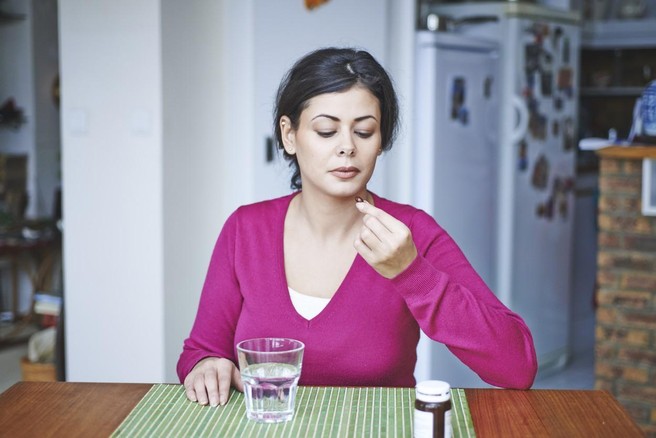 Ženska v roki drži vitaminski dodatek.