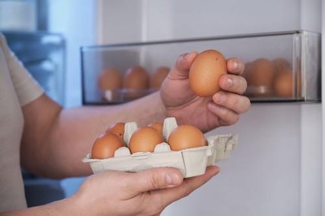 Moški shranjuje jajca v hladilnik.
