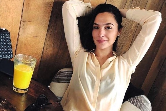 gal gadot sedi na stolu in pije sok