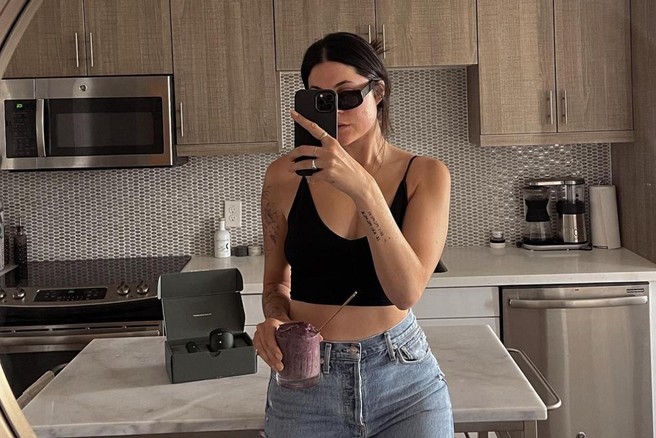 Ženska v ogledalu dela selfie in v rokah drži smoothie