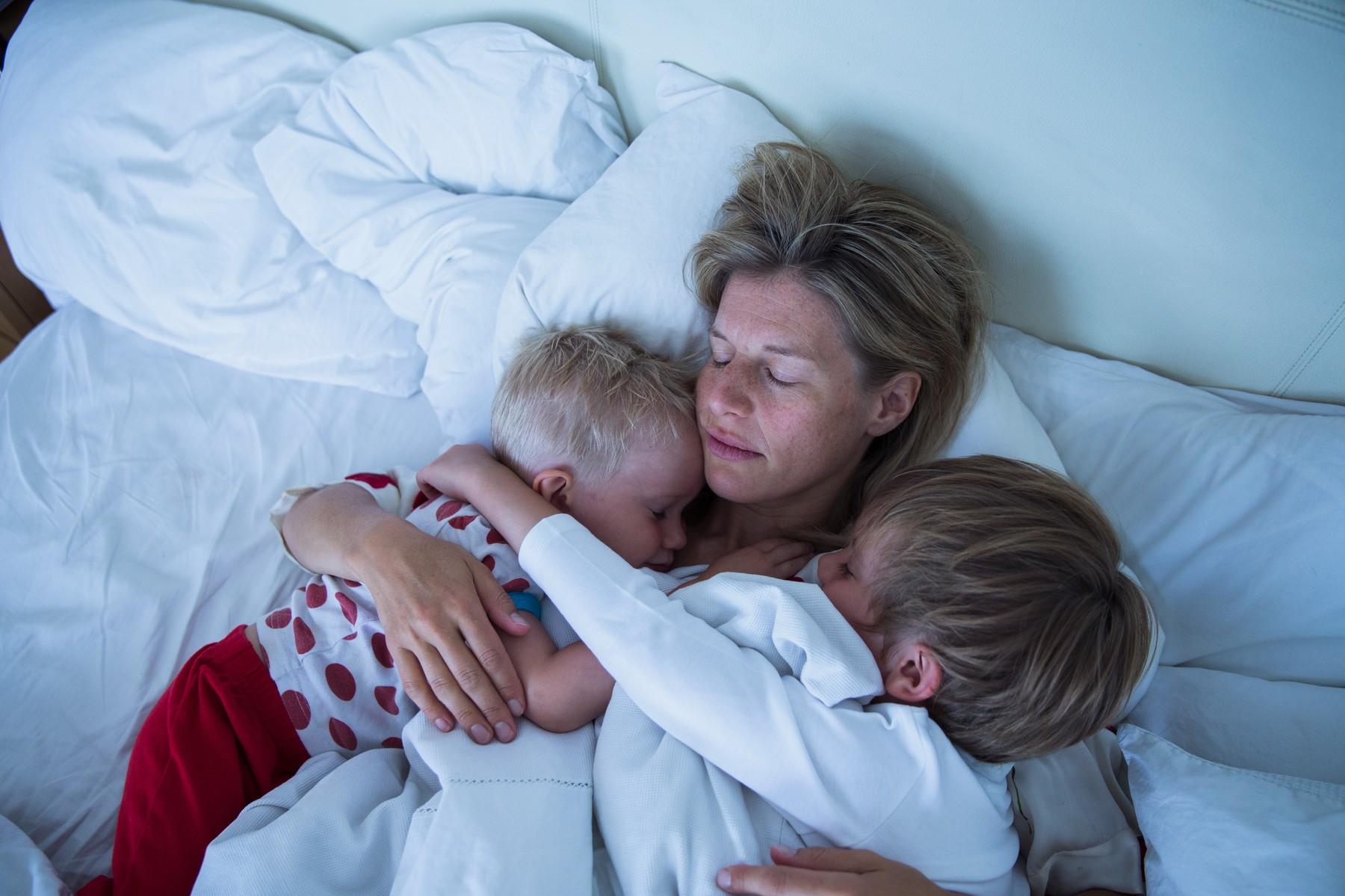 Mama z dvema majhnima sinovoma leži na postelji.